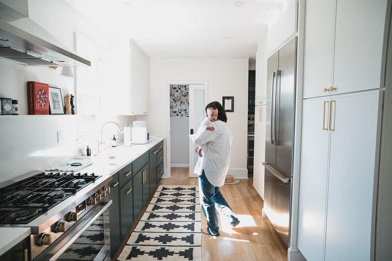A mother holding her baby in a bright kitchen during an in-home family photography session, captured by Connecticut family photographer Rebecca Bloomfield with a candid, documentary feel