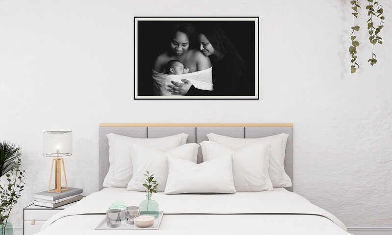 A framed image of a newborn baby hands above a white bed
