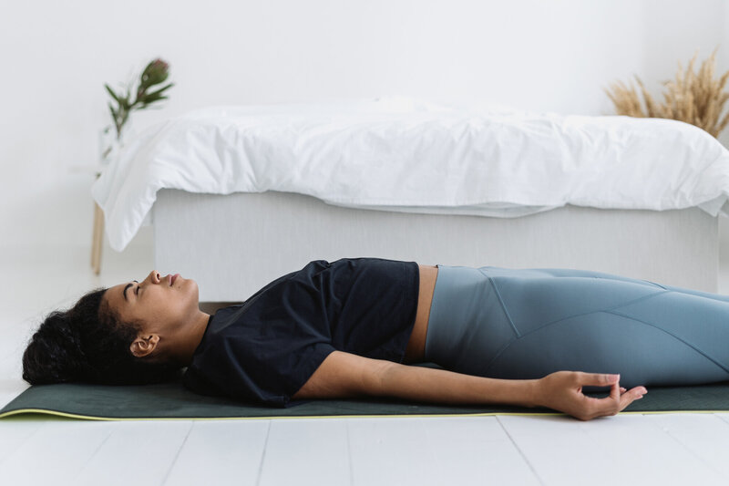 Woman lying on a yoga mat in her room, practicing a body scan.