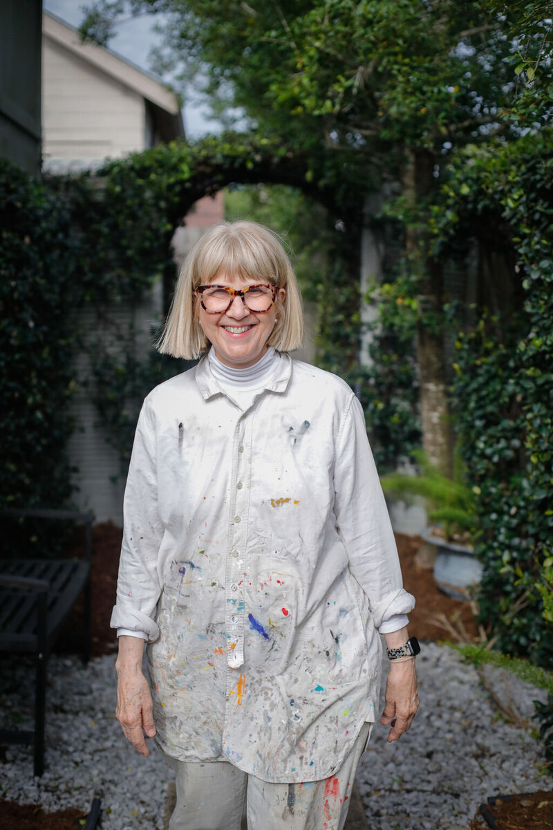 Adele walking in overgrown garden wearing paint covered artist smock