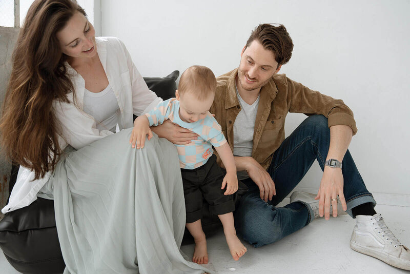 male and female with baby boy on black leather chair in all white studio