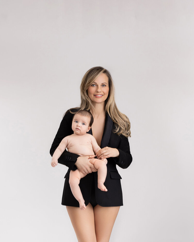 Indoor London Beckenham studio portrait of a smiling standing mother holding her baby