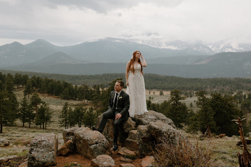 bride and groom sitting on rocks with mountains in the background