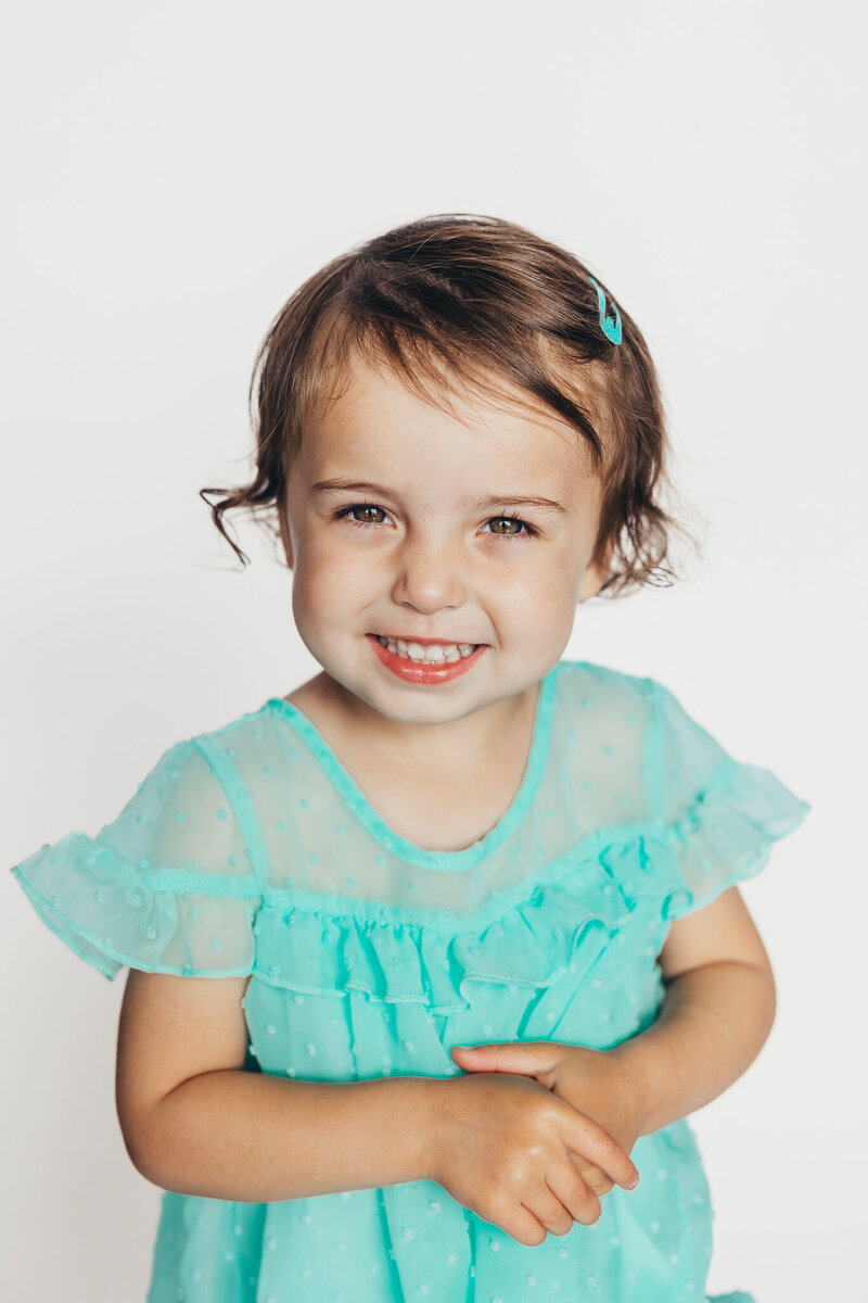 A sweet preschool aged girl smiles in front of a crisp white background