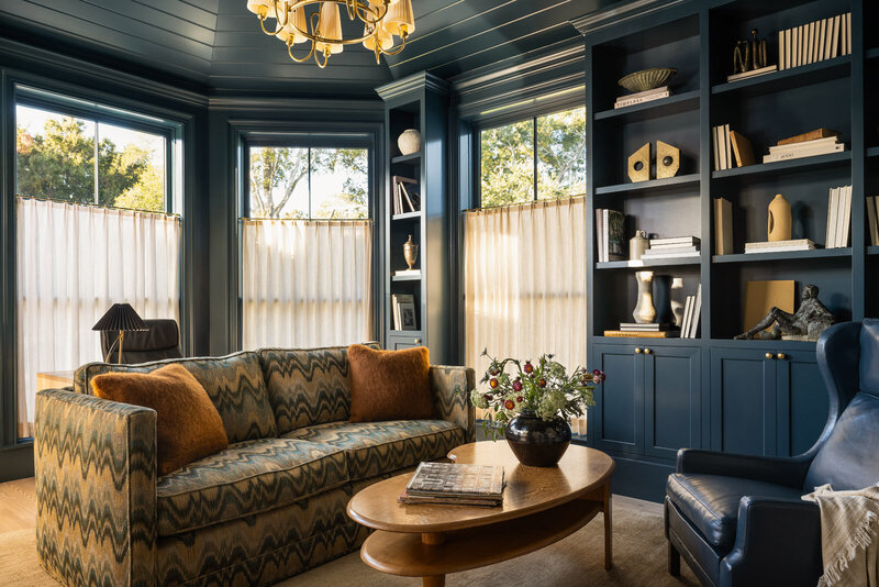Bold living room with beige couches, green velvet ottoman and patterned artwork