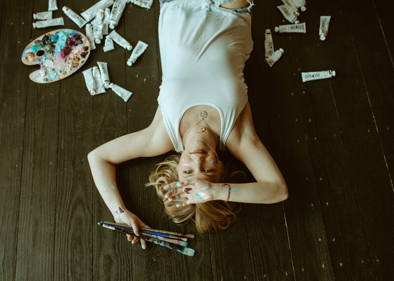 woman laying on the ground with paint and brushes