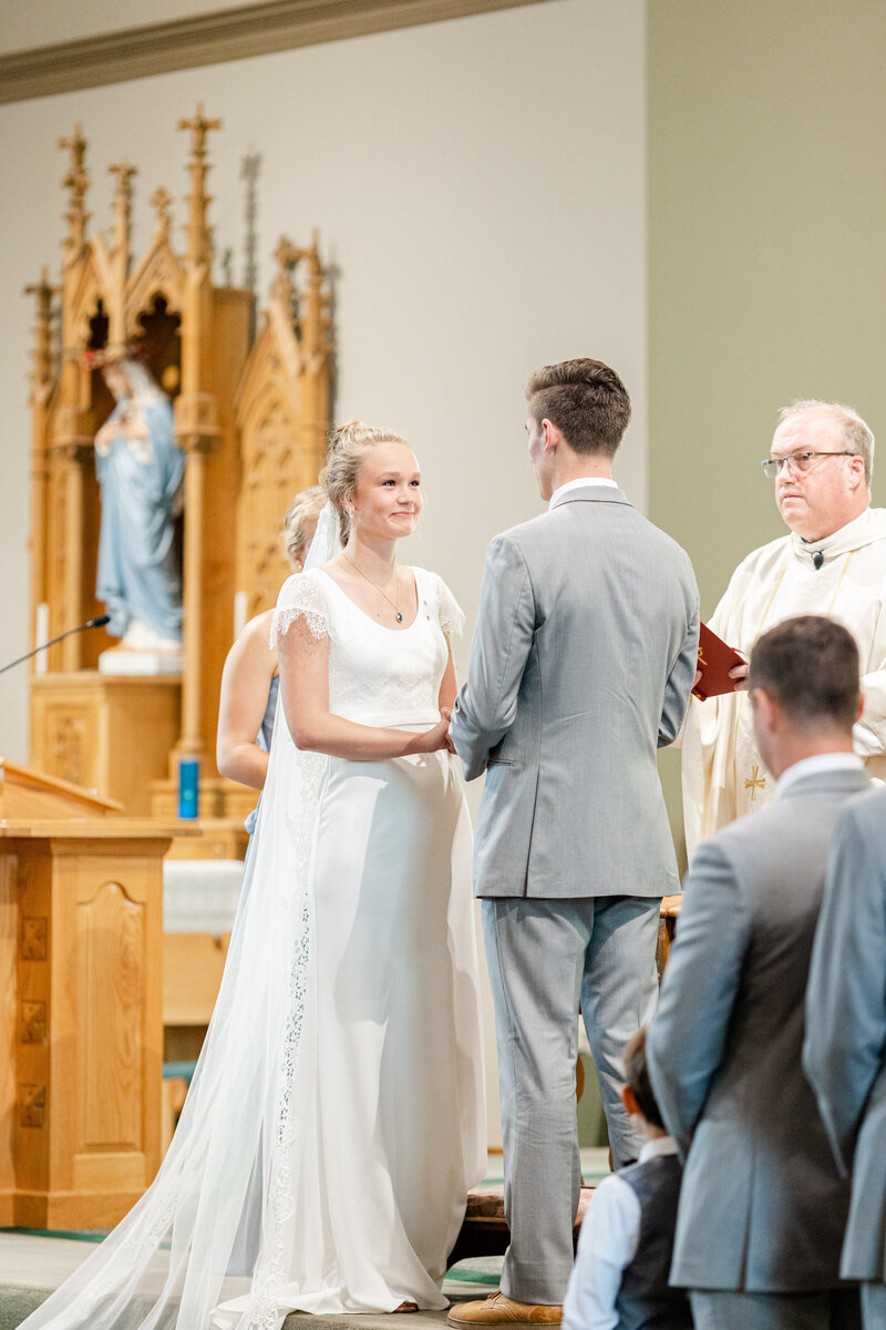 Bride and groom hold hands during their wedding vows at a catholic wedidng mass in York, Nebraska