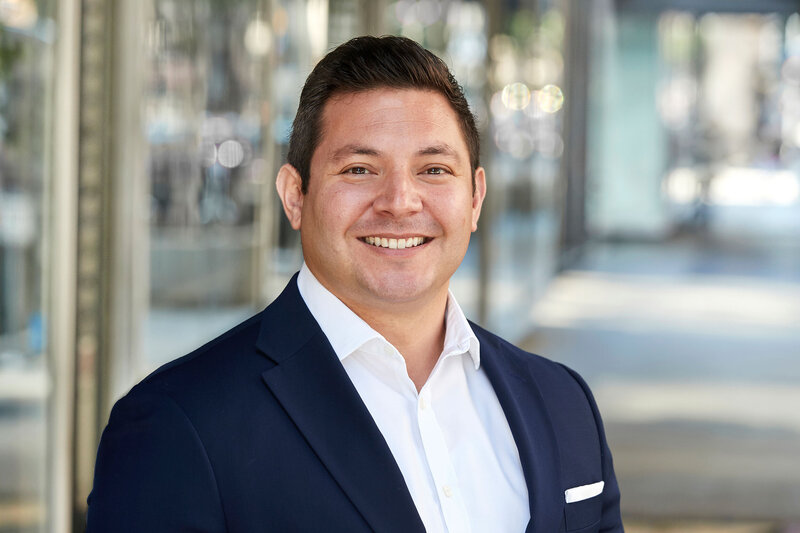Professional outdoor portrait of Nick Lara in a dark suit, smiling confidently, captured by Ylva Erevall.