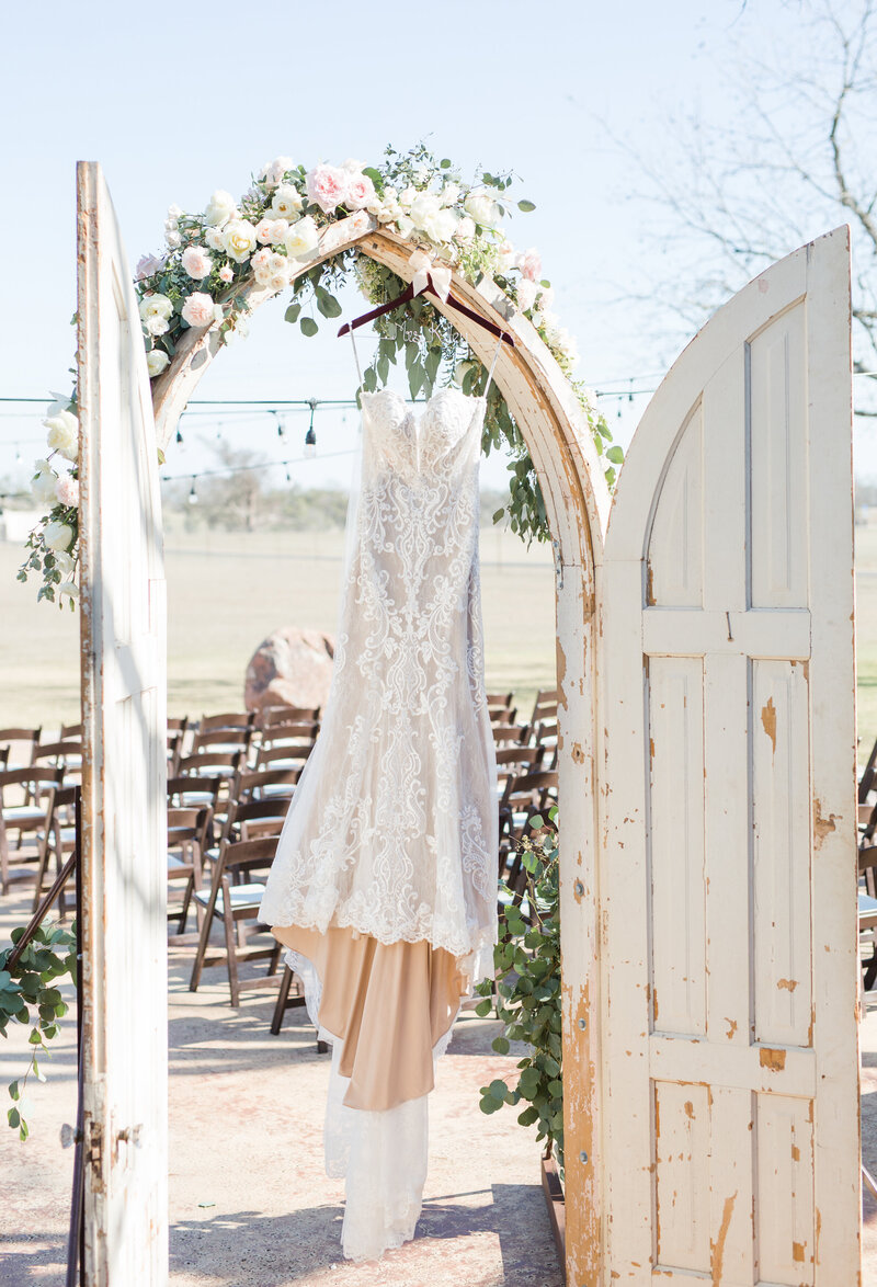 A lace wedding gown hangs gracefully on an outdoor archway, symbolizing the elegance and attention to detail provided by Socially Significant Events.
