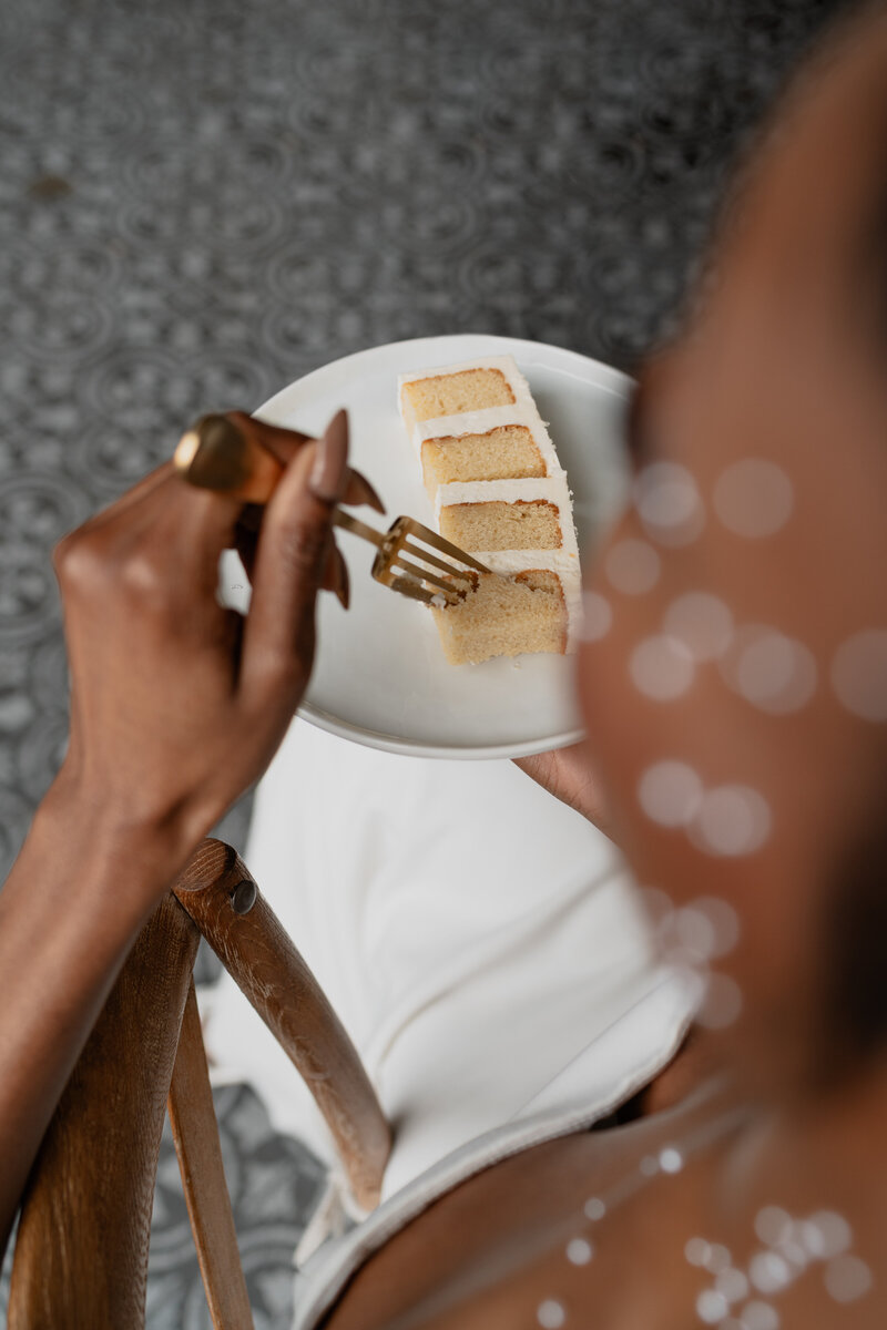 back view of a bride sinking her fork into a piece of wedding cake