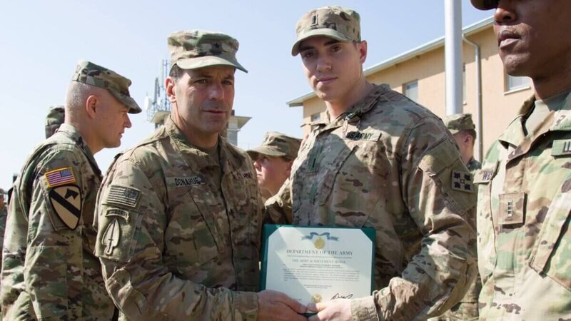 U.S. Army soldiers in uniform during an award ceremony, with one soldier receiving a certificate from a commanding officer.