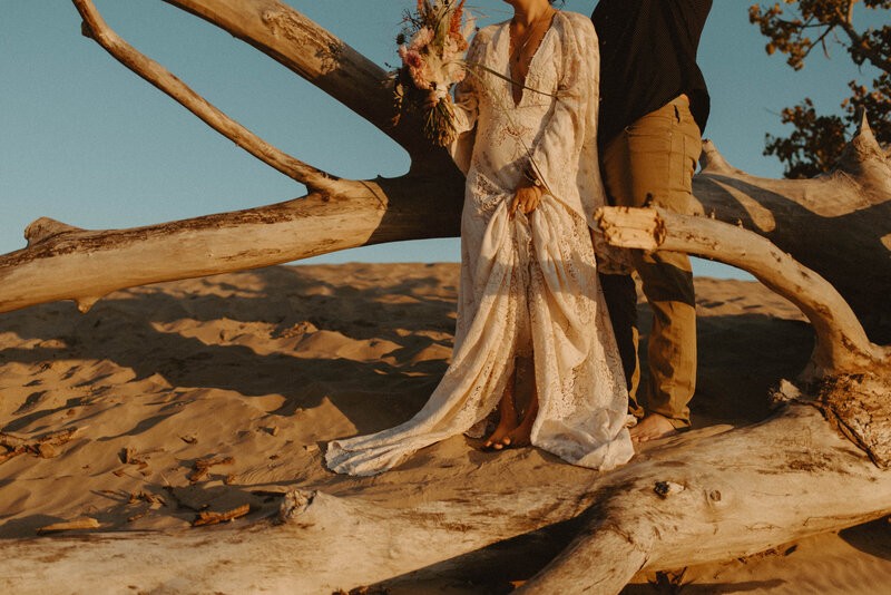 bride and groom standing on sand dunes at sunset
