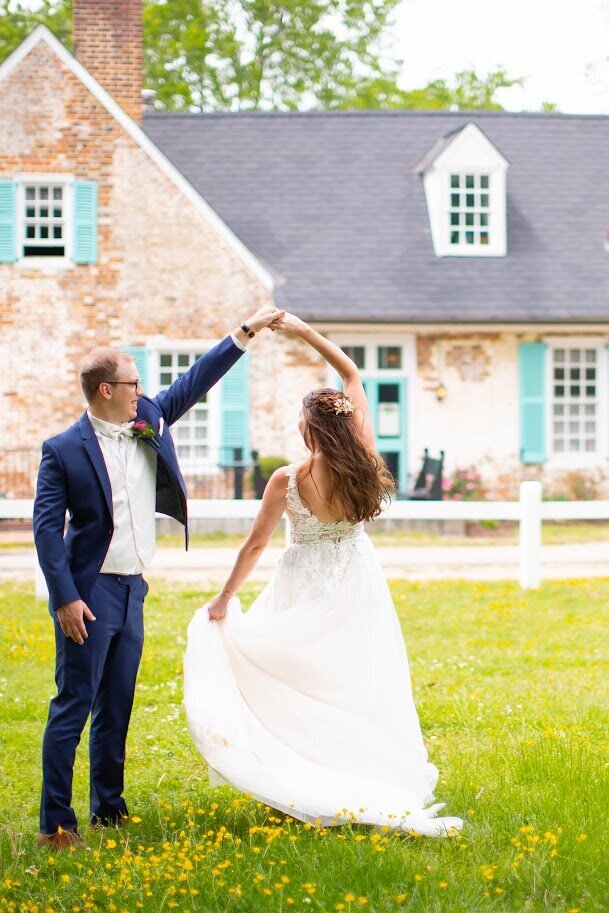 Bride and groom dancing and twirling in front of a Colonial building in Yorktown, Virginia, during their wedding, coordinated by Sweet Caroline Events