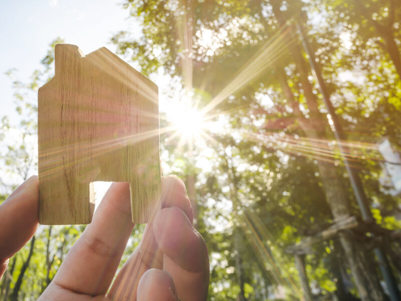 hand holding model of a home outside with sun streaming through the trees