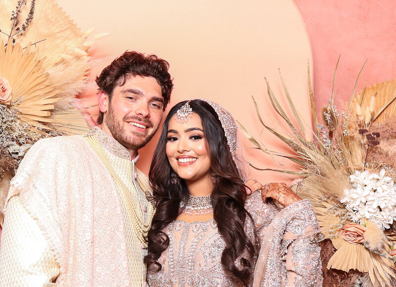 An elegant bride and groom posing a floral premium backdrop during an Asian wedding celebration, with Mad Hat Premium Photo Booth hire for luxury Asian Weddings