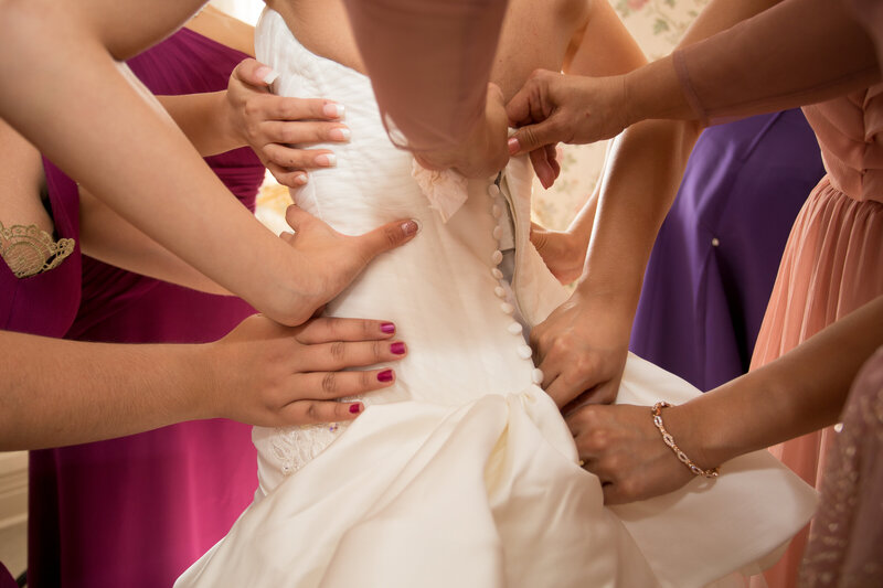 Bridesmaids help the bride zip the back of her wedding dress.