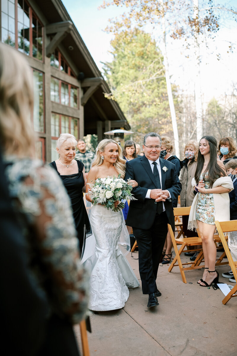 Portrait of bride and her parents walking down the aisle to her ceremony at Donovan Pavilion in Vail Colorado.