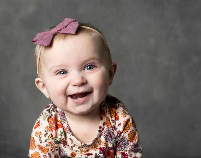 A baby smiles looking right at the camera.
