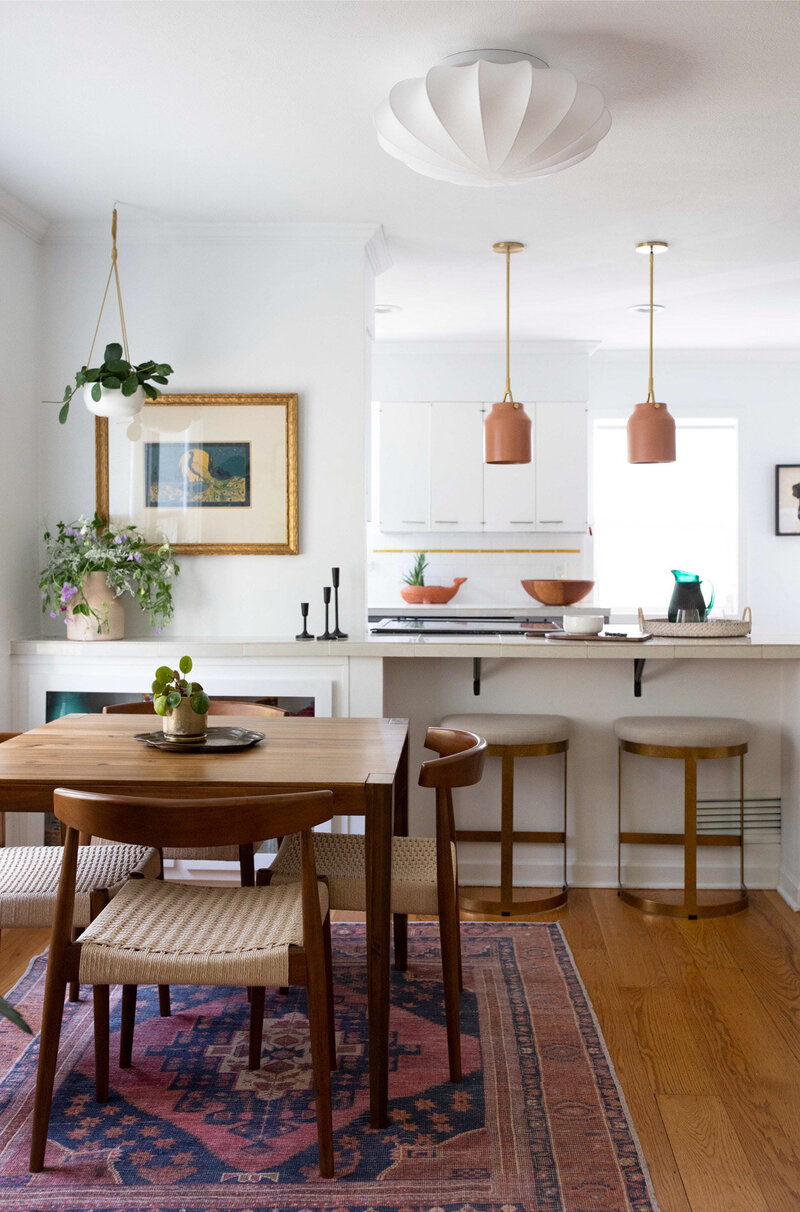 A dining room table on top of a patterned rug, and a look into the kitchen behind it representing an example of art deco boho interior design.