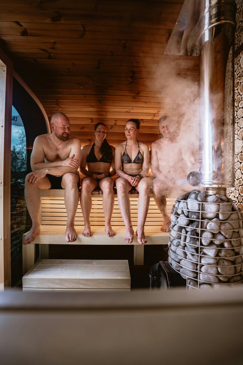 Three people relaxing in wooden sauna at Vitalis wellness studio with traditional sauna heater