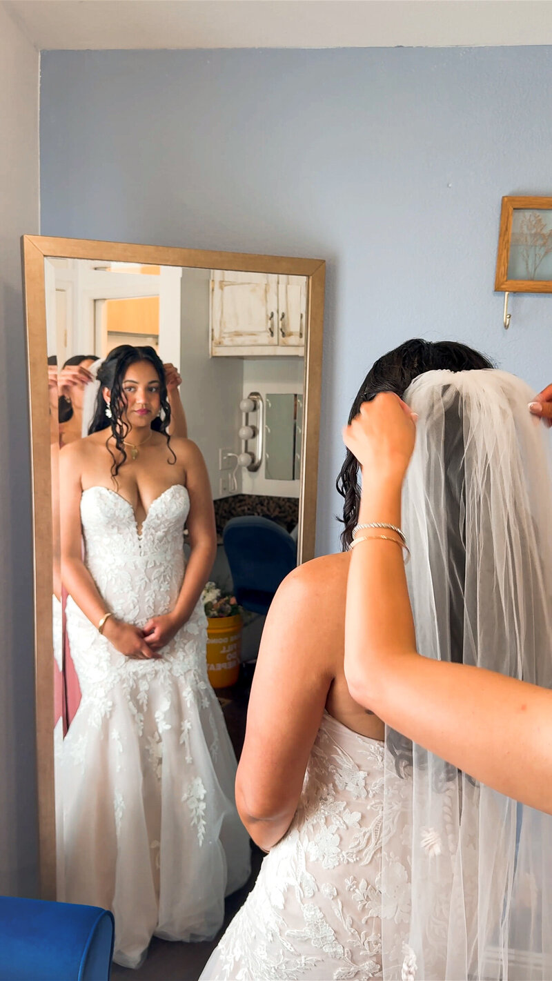 Maid of honor helping the bride put on her long veil in the mirror in the getting ready room at The Orchard Wedgewood Weddings.