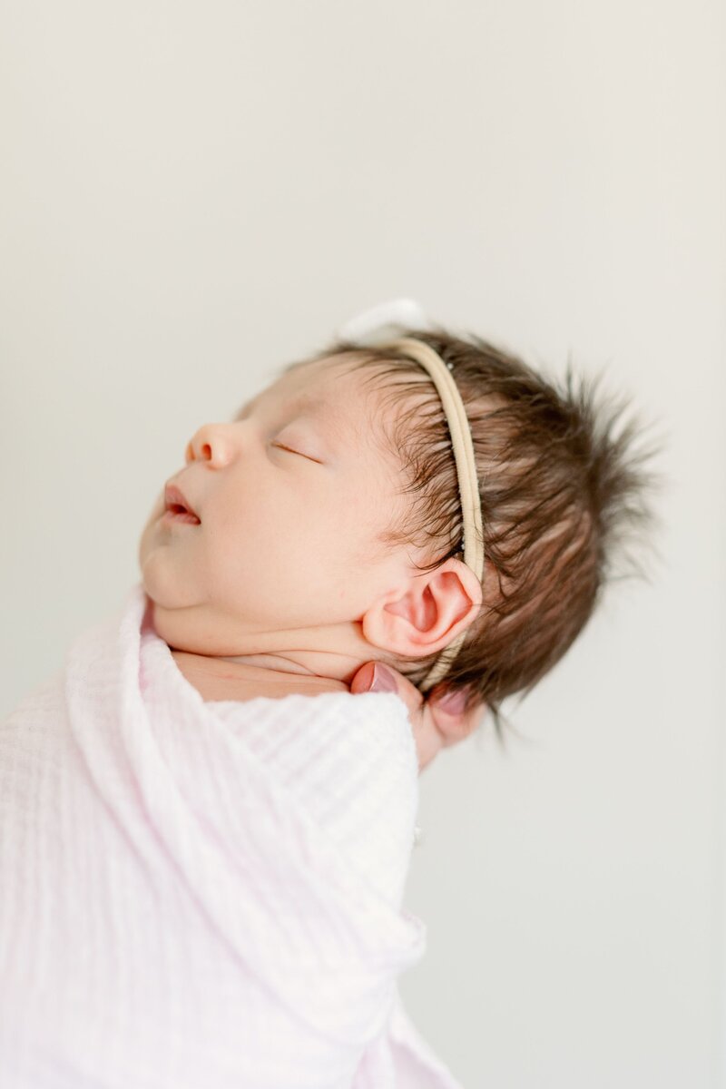 A delicate newborn baby sleeps soundly, swaddled in soft, neutral tones. The serene expression and gentle lighting create a timeless and heartwarming newborn portrait, embodying the pure innocence of early life. Photographed by KCP Families.