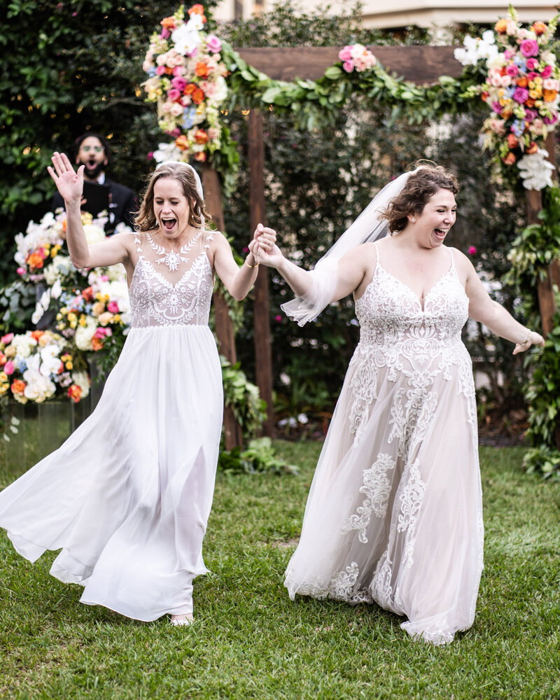 Brides laughing as they walk out at the end of wedding ceremony at The Elms Mansion in New Orleans