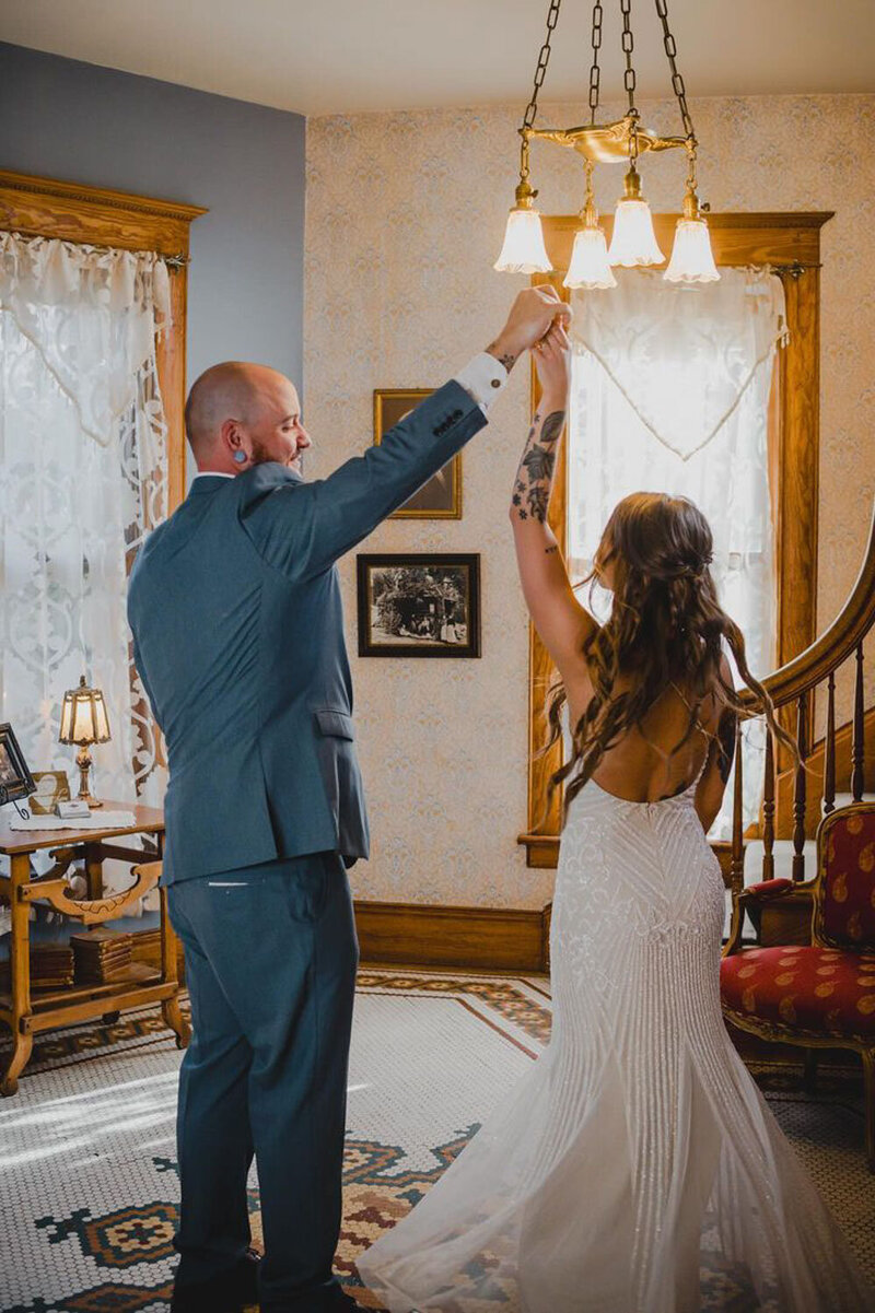 Groom twirling the bride in an elegant room with vintage decor and soft lighting