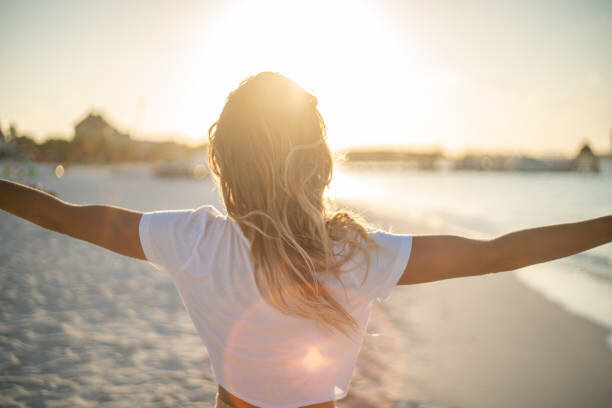A woman with arms open lookin gout at the beach feeling liberated