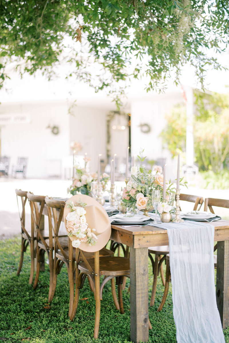 bright and airy photo of natural rentals staged at Southern Grace venue in FLorida with soft and light florals decorating the table and chairs with a tree hanging over the setting