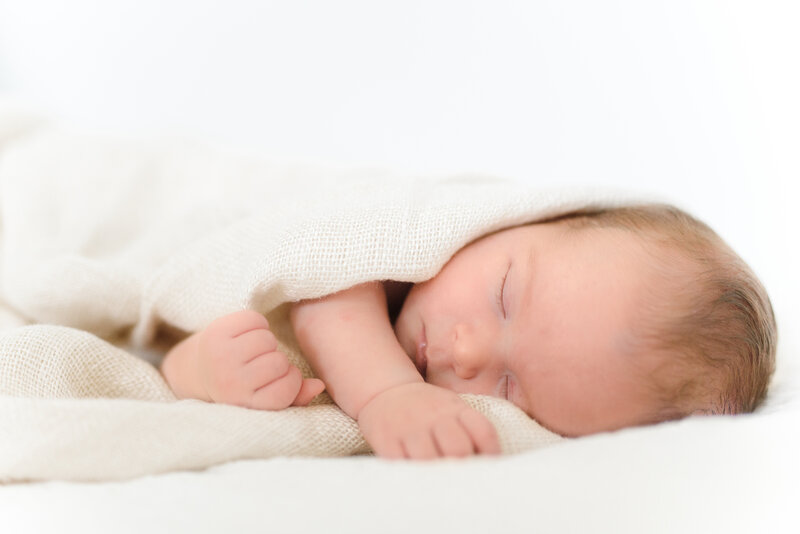 Ansiktet og hendene til en nyfødt baby som ligger på siden og sover