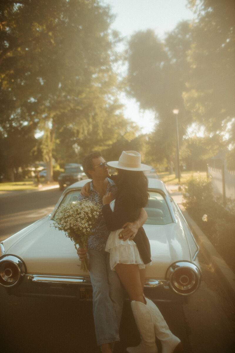 bride and groom embracing while sitting on classic car