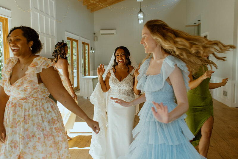 bride laughs with bridesmaids dancing around room