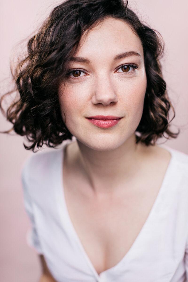 Casting headshot van actrice met kort bruin haar voor een roze achtergrond.