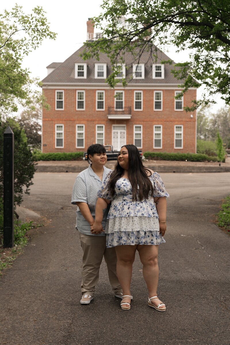 Engaged couple holding hands in front of a brick mansion at Coxhall Gardens, Carmel, Indiana