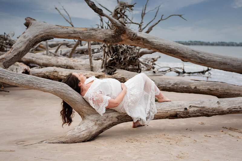 Maternity portrait of pregnant mom in white dress lying on driftwood at Talbot Island,