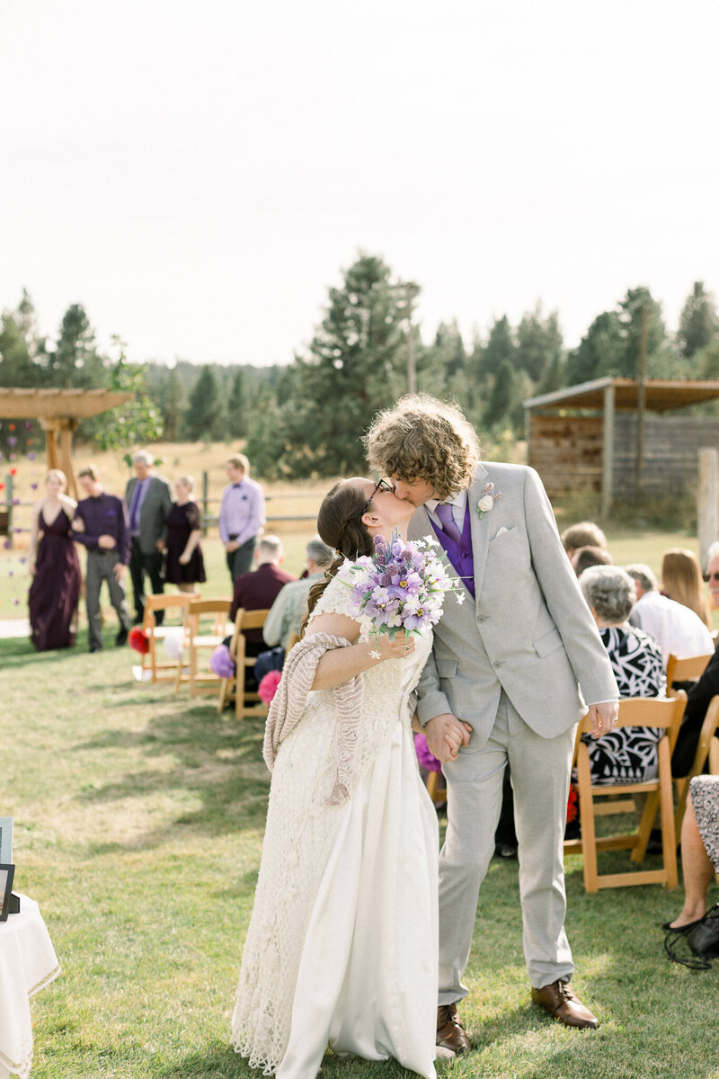 Bride and groom sharing a kiss at the end o the aisle taken by Spokane Wedding Photographer