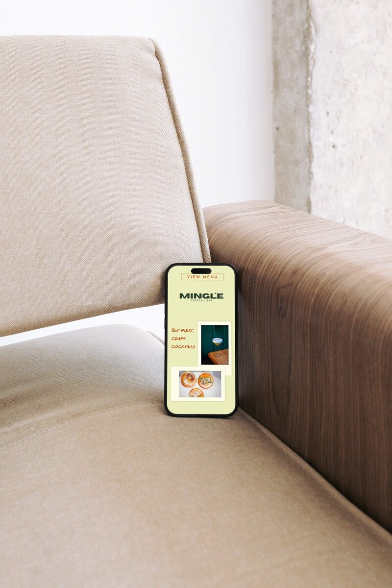 iPhone on chair, displaying a website for a cocktail bar