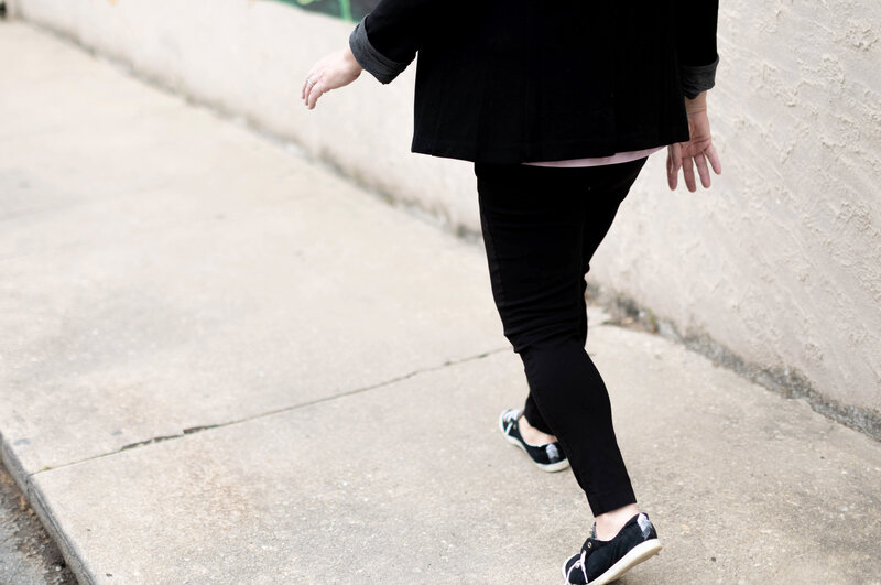 Jaymi walking on the sidewalk wearing a black blazer and black pants