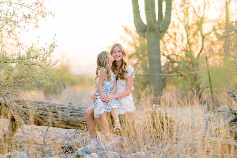 sisters sitting down in the arizona desert with the younger sister giving the older one a kiss