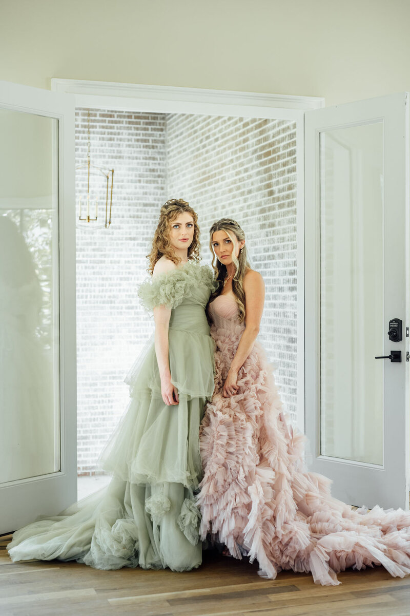 Two women in ruffled gowns posing by glass doors