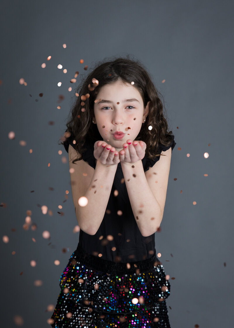 Girl blowing sparkly glitter with bokeh at the camera at Allison Reilly's Union County, NJ photo studio.