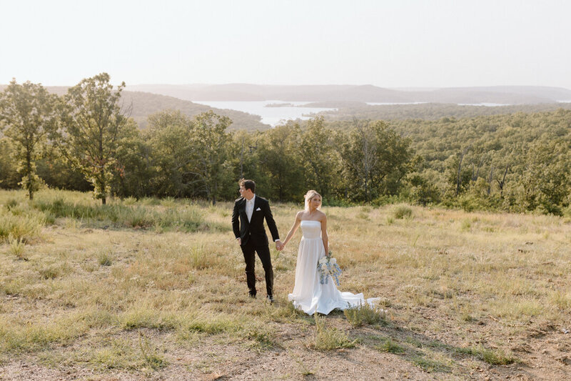 A wedding couple holding hands in a field.