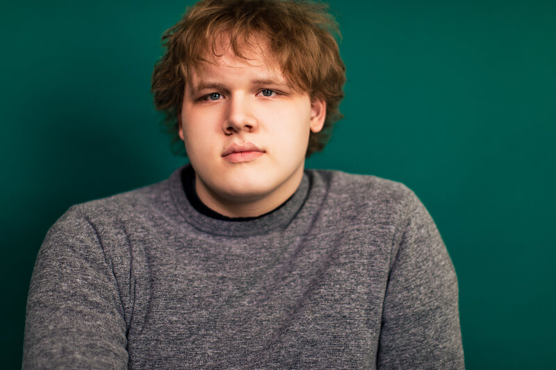 a red haired boy wearing a grey sweater stands out boldly from a kelly green background in this studio portrait.
