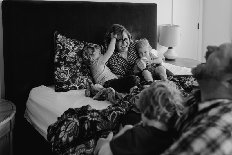 Family Photographer, a mother snuggles her toddlers in bed laughing
