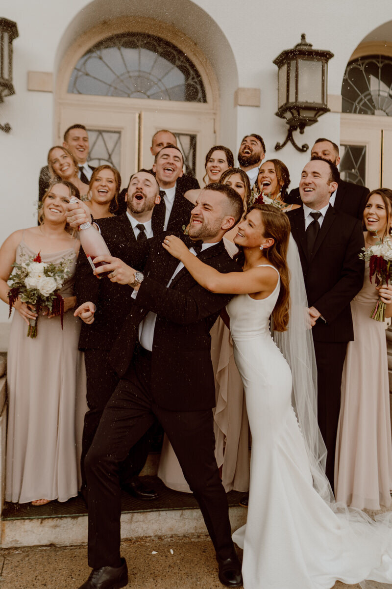 bride and groom popping champagne with bridal party