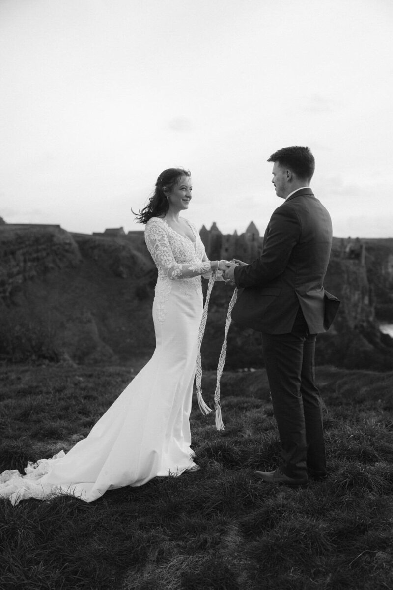 Eloping couple performs a handfasting unty ceremony idea in front of Dunluce castle in Northern Irelands