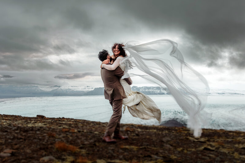 Married couple is dancing on top of a mountain with epic glacier view in the background in Iceland