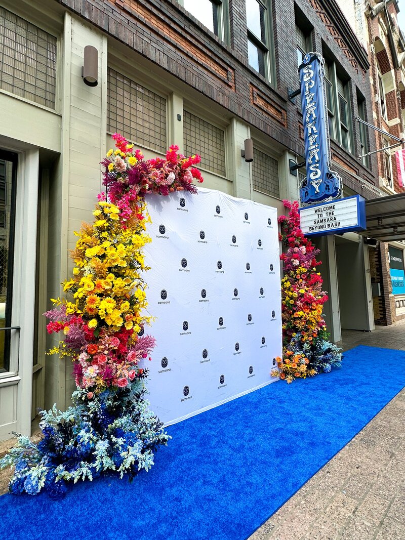 Vibrant corporate event photo backdrop with colorful florals and blue carpet, designed for Austin brand activations.