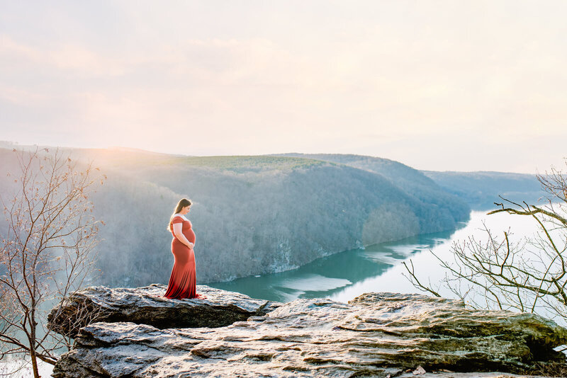 A pregnant woman standing on a rock overlooking a cliff with water below.